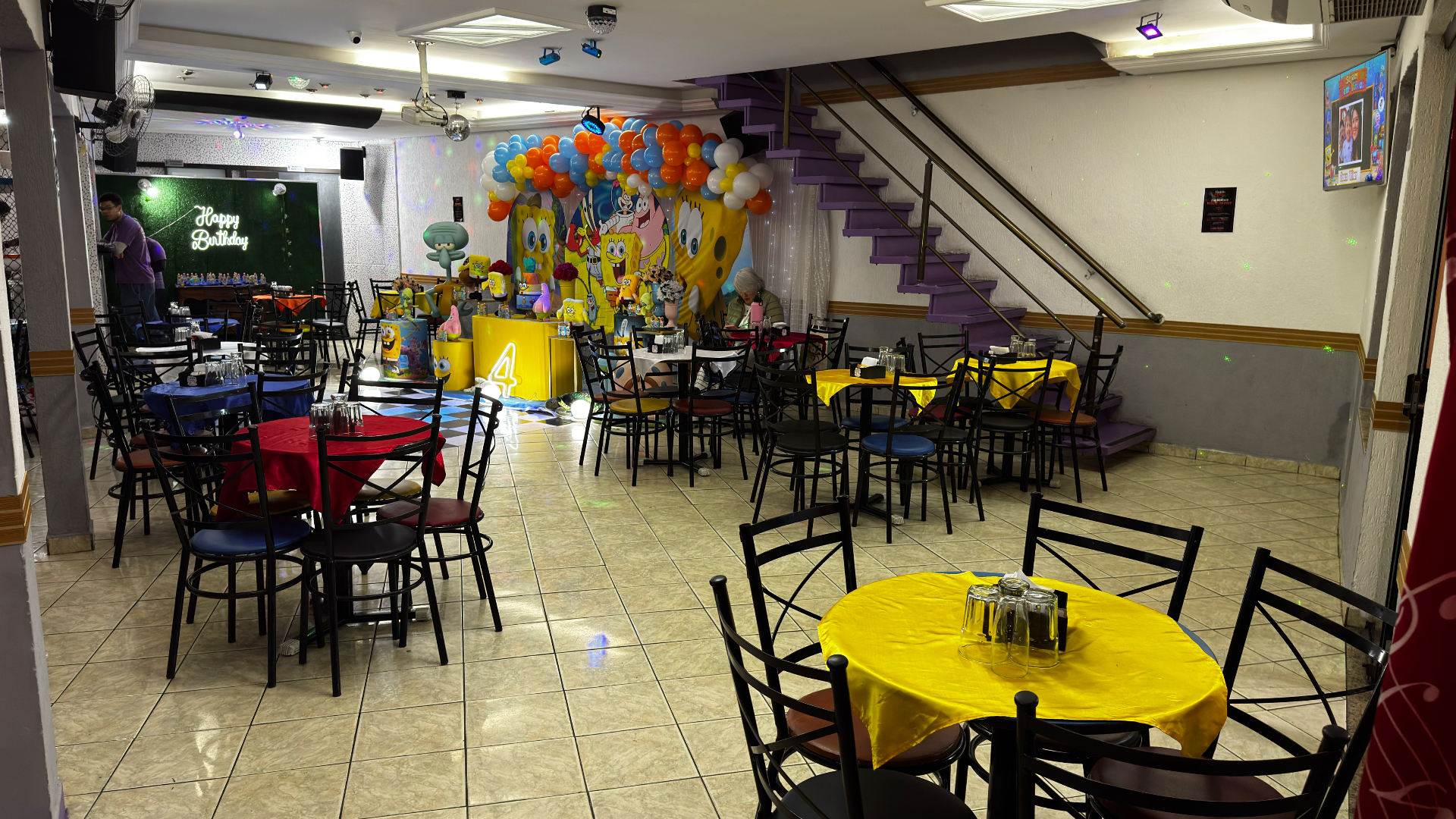 Escada e ambiente do salão principal do Castelo Mágico Buffet Infantil, com mesas coloridas