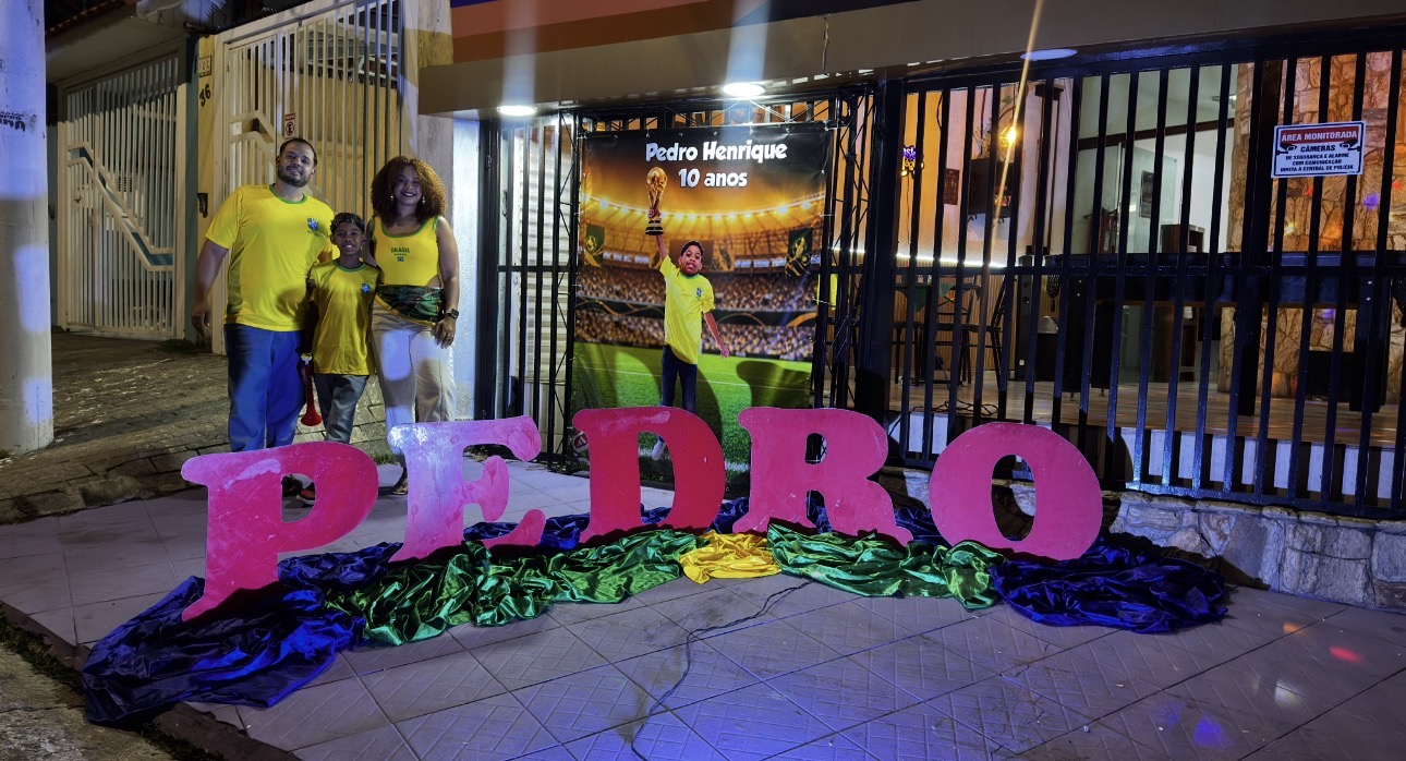 Família comemorando na entrada do Castelo Mágico Buffet Infantil, com letras decorativas do nome do aniversariante e painel personalizado da festa