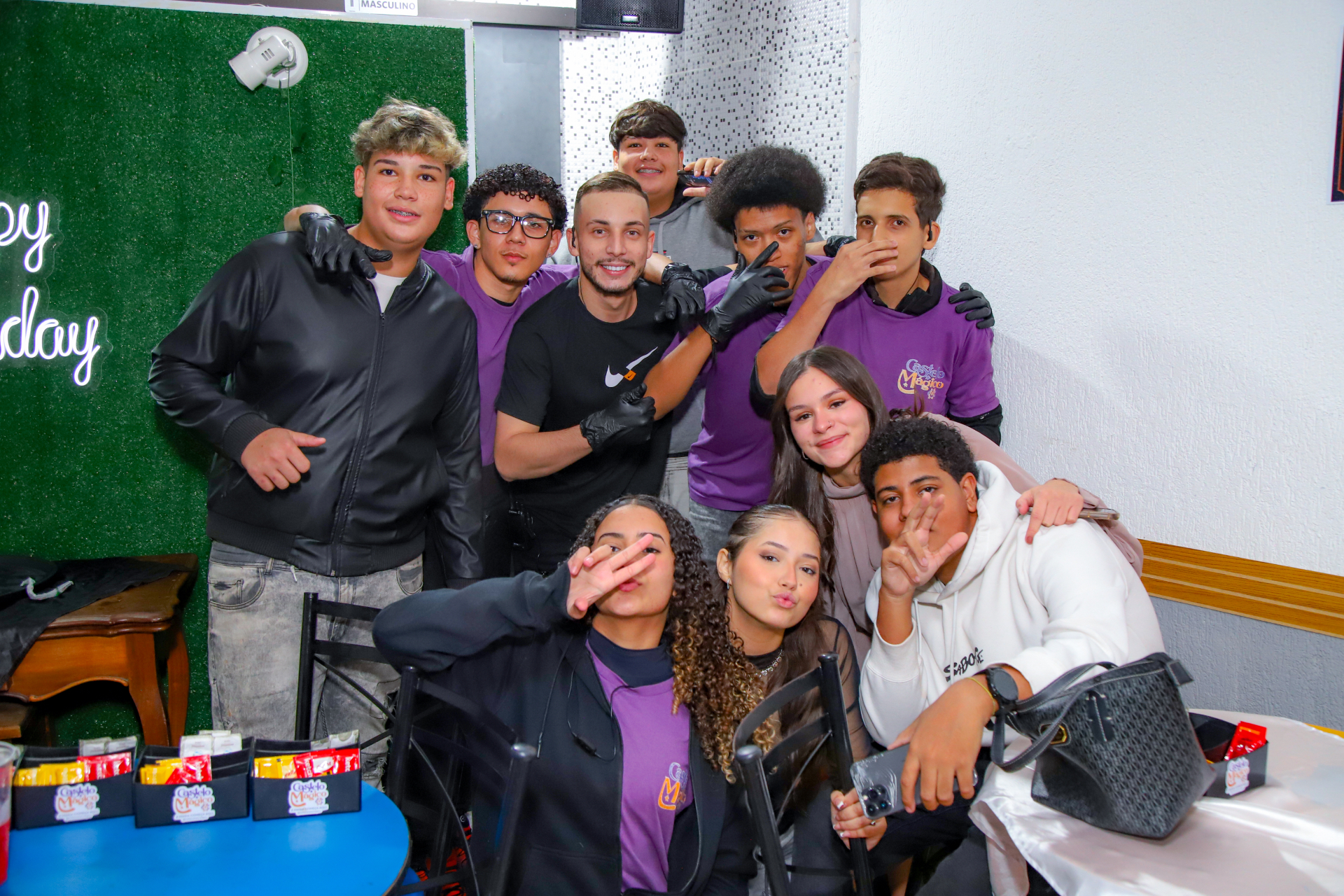 Equipe do Castelo Mágico Buffet Infantil reunida em uma festa, com a camiseta roxa do buffet e o letreiro neon de happy birthday ao fundo