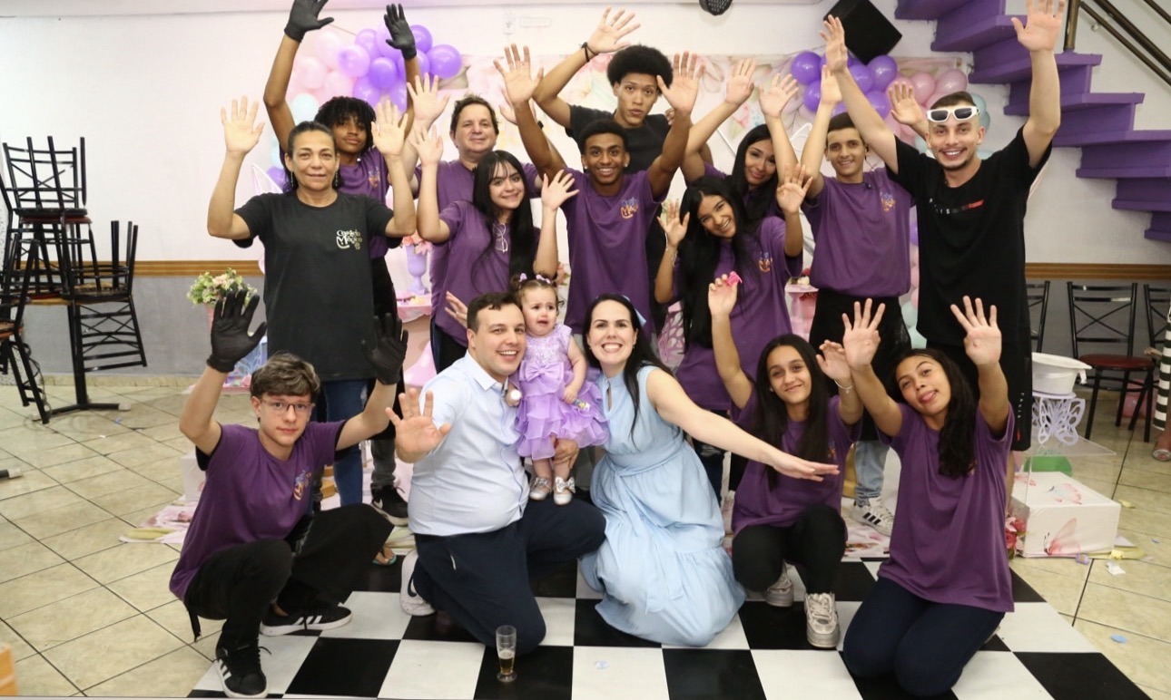 Equipe do Castelo Mágico Buffet Infantil comemorando durante uma festa, de mãos erguidas, com decoração de balões ao fundo