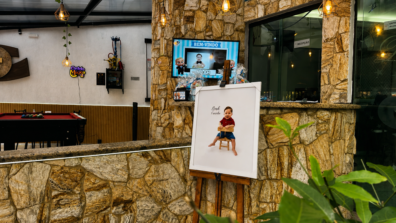 Recepção do lounge do Castelo Mágico Buffet Infantil, com painel de boas-vindas na TV e quadro do aniversariante em cavalete