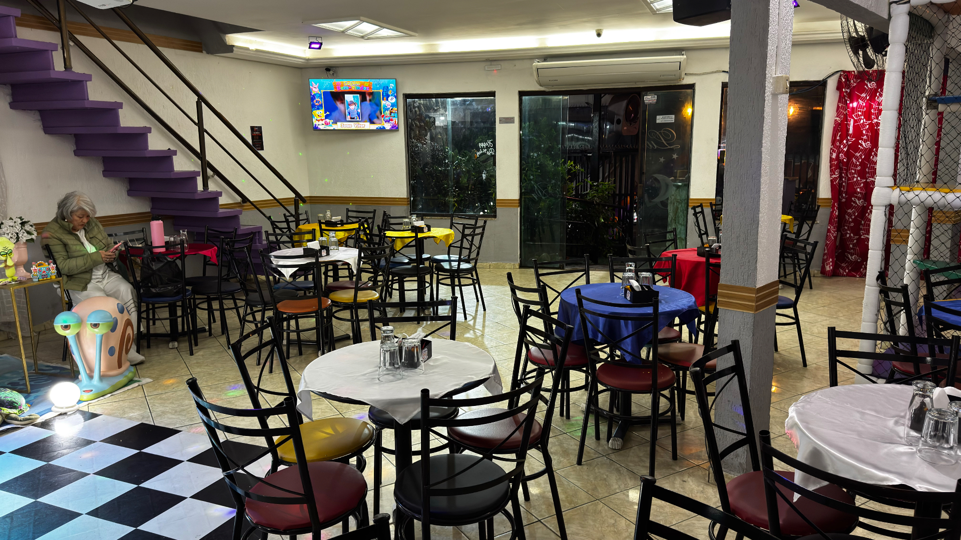 Vista do ambiente do salão principal do Castelo Mágico Buffet Infantil, com mesas e brinquedos ao fundo