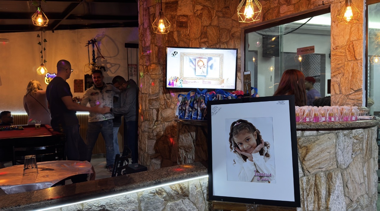 Decoração de recepção de festa no Castelo Mágico Buffet Infantil, com quadro do aniversariante em cavalete, lembrancinhas e painel personalizado na TV